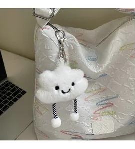 Close-up of a white plush cloud keychain with a smile face attached to a tote bag