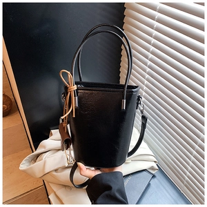 Close-up of black leather bucket bag with double handles and detachable silver strap