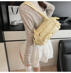 Detail of a creamy yellow PU leather pillow bag with glossy finish and decorative buckles