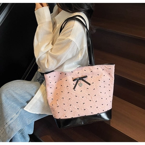 Dettaglio della borsa tote rosa a pieghe con fiocchi neri e ciondolo a cuore indossata