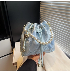 Detailed shot of light blue lace bucket bag with pearl handle and chain strap
