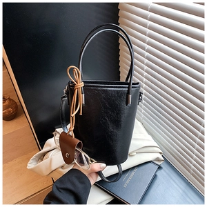 Close-up of black glossy leather bucket bag with retro knot charm and glasses detail