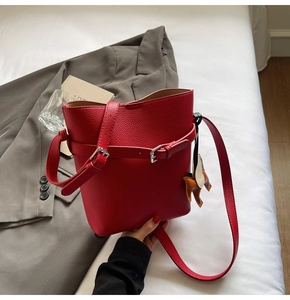 Close-up of red lychee textured bucket bag with leather horse charm on white linen