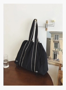 Detail of a large capacity black tote bag with contrast woven straps hanging on a wall