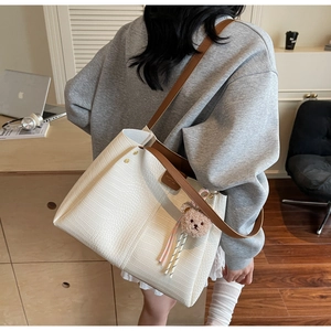 Detail of ivory tote bag featuring crocodile texture, brown straps and a cute bear charm