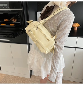 Detail of beige faux leather crossbody bag with buckle and zipper pockets on a table