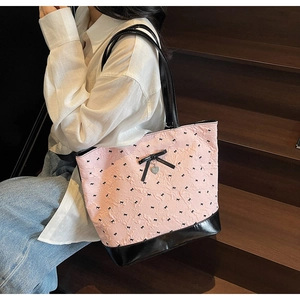 Dettaglio borsa tote rosa con fiocchi neri e ciondolo a cuore su scale di legno scuro