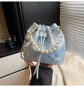 Detailed view of light blue bucket bag with floral jacquard, pearl handle, and butterfly