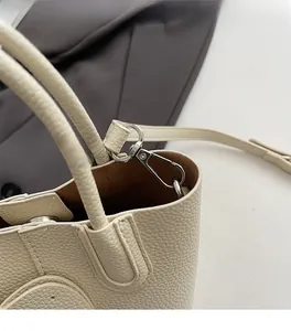 Detail of off-white lychee grain leather handbag showing silver metal strap buckles