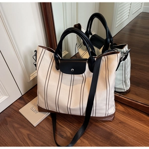 Close-up of a striped canvas tote bag featuring leather handles and detachable crossbody strap