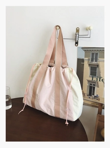Detail of a large pink and beige canvas tote bag with drawstring closure hanging on a wall
