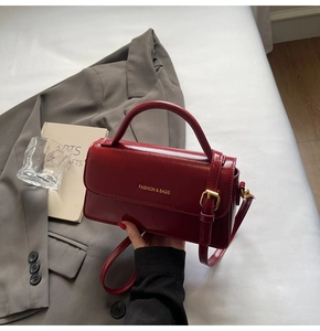 Detail of deep red leather crossbody bag with gold fashion lettering and handle
