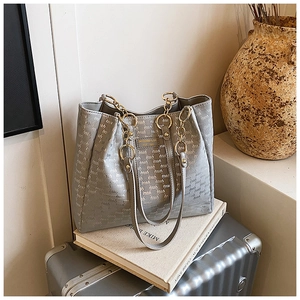 Détail du sac cabas gris monogramme avec anses en chaîne dorée sur une valise