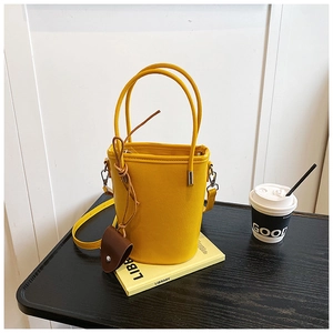 Detailed view of yellow leather bucket bag with top handles and adjustable strap on a table