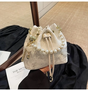Detail view of white floral lace bucket bag with pearl handle and golden chain strap