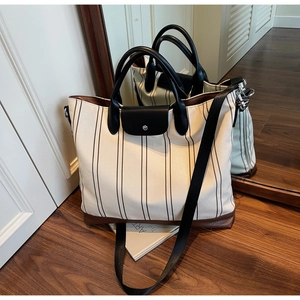 Detail of striped canvas tote bag with brown leather trim and black handle in a room