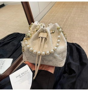 Detail of white lace bucket bag featuring pearl handle and golden chain strap for wedding