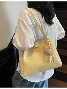 Large pale yellow tote bag with crocodile pattern and bear charm shown on model