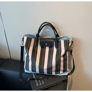Detail of striped canvas tote bag in pink and green with black leather handles on sofa