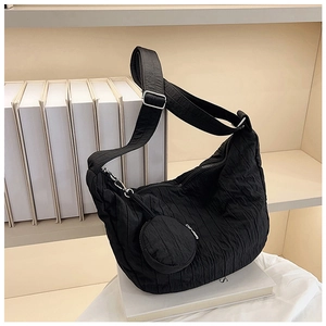 Detail of black pleated crossbody bag with matching round pouch on a white magazine