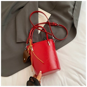 Detail of red bucket bag with synthetic leather texture, side knots and crossbody strap
