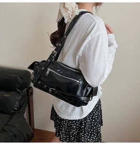 Detail shot of black glossy shoulder bag with metallic zippers and eyelet straps