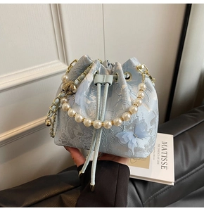 Detail of light blue bucket bag with floral brocade, pearl handle, and butterfly decor