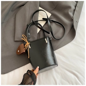 Detail of black leather bucket bag with brown charm and adjustable shoulder strap