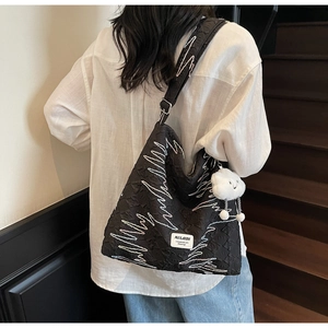 Detail of black tote with wavy embroidery and a white cloud plush charm on strap