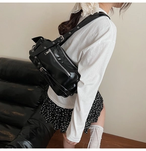 Detail of a black patent leather punk crossbody bag with metallic eyelets and straps