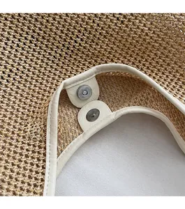 Detail of magnetic buckle closure with beige faux leather trim on straw woven tote bag