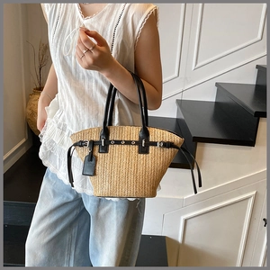 Close-up of woven straw tote bag with black leather straps and silver buckle detail