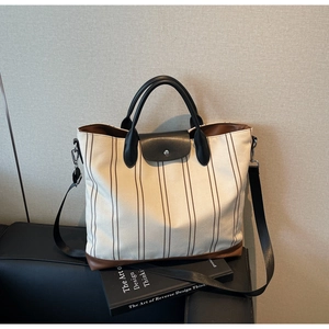 Detail of striped canvas tote with leather trim, metal buckle, and wide shoulder strap