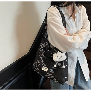 Detail of black quilted tote bag with wave stitching and white plush cloud pendant