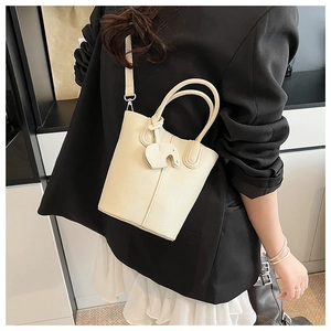 Detail view of cream bucket bag with lychee texture and elephant charm on model