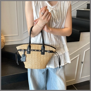 Close-up of woven straw tote bag featuring black leather handles and metal eyelet trim