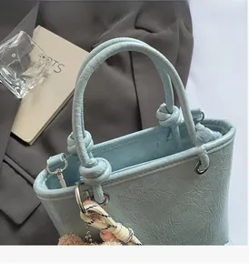 Detail of light blue pleated faux leather tote bag with decorative bear charm and knot handle