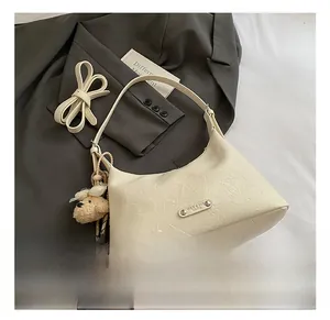 Détail d'un sac en cuir plissé crème avec logo métallique et pendentif ours en peluche