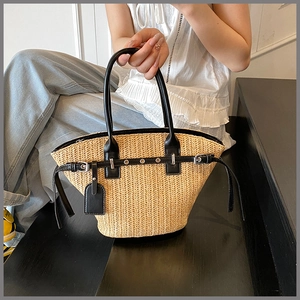 Close-up of woven straw beach bag featuring black leather straps and metal eyelets