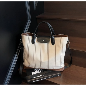 Close-up of large striped canvas tote bag with leather flap and metal buckle on wooden stairs