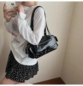 Detail of glossy black shoulder bag featuring metallic zippers and eyelet straps