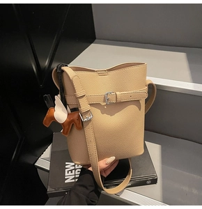 Close-up of beige litchi grain bucket bag with leather strap and horse charm detail