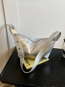 Sac hobo demi-lune argenté avec large bandoulière à œillets sur livre jaune