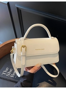 White leather handbag with gold hardware and top handle shown on a black backdrop