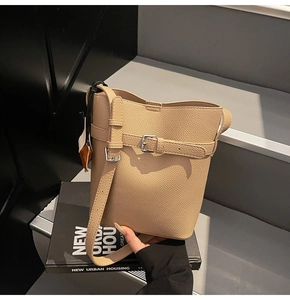 Detailed view of beige lychee pattern leather bucket bag with silver buckle on books