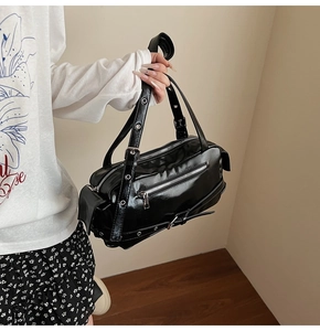 Detail of black glossy handbag featuring silver zippers and metallic eyelet straps