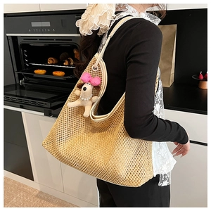 Detail view of woven straw tote bag featuring a cute plush dog charm with pearl necklace