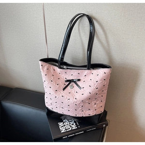 Dettaglio della borsa tote rosa con ricamo a fiocco nero e ciondolo metallico a cuore
