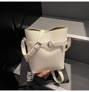 Close-up of white lychee pattern leather bucket bag with silver metal belt buckle detail