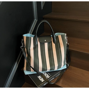 Detail of striped canvas tote bag with leather handles and flap on wooden stairs